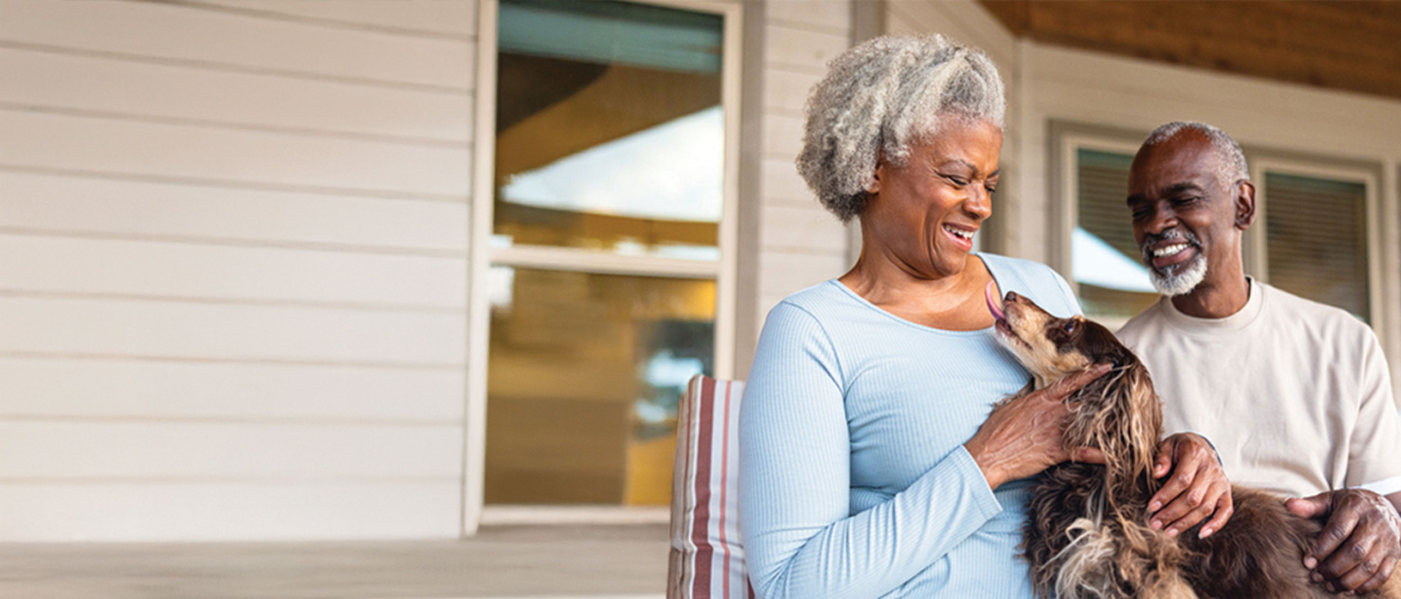 Smiling older couple sitting on a porch, laughing while petting their small dog